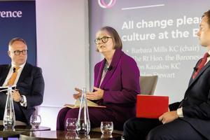 A photo of three people on stage, Harriet Harman is speaking, Leon Kazakos and Lachlan Stewart are listening