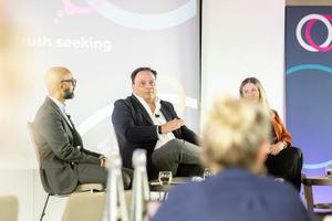 A photo of three people on stage, Jason Beer KC is speaking, Haroon Siddique and Kate Eves OBE are listening